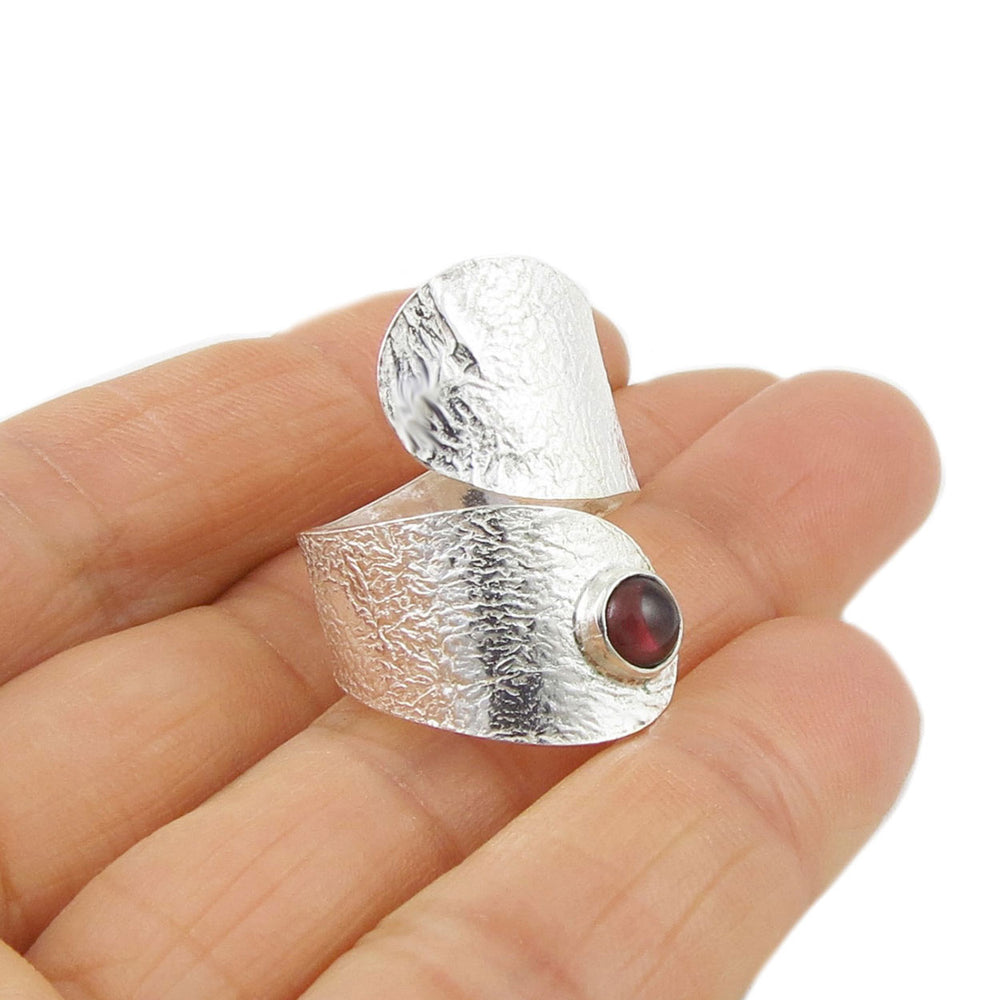 Crumpled sterling silver spiral ring with a red garnet gemstone held i a person's hand.