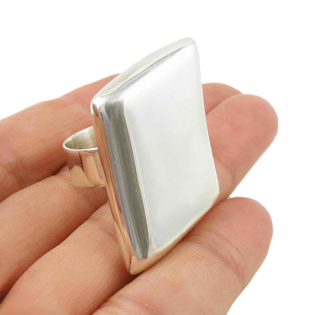 Silver ring with a geometric rectangle design held in a hand on a white background