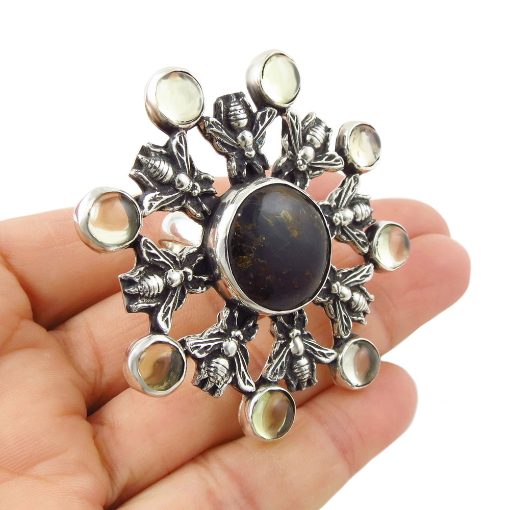 A large handmade silver ring with a UK hallmark decorated with natural amber gemstones held in a persons hand. 