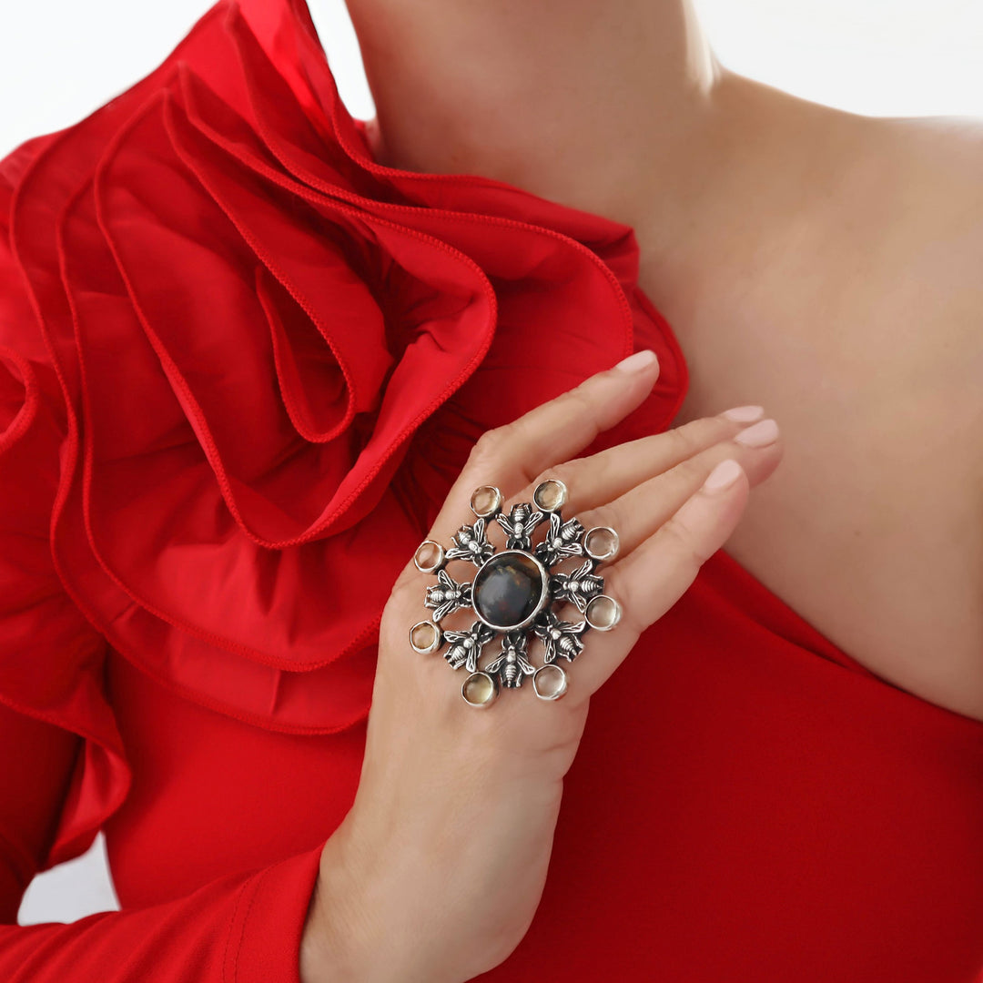 A woman in a red dress with a wide frill wearing a large silver cocktail ring decorated with amber gemstones