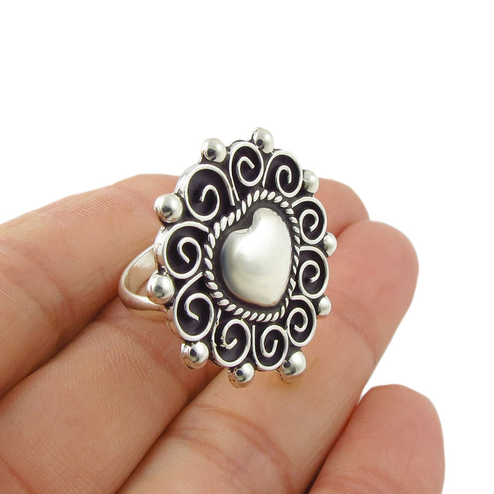 Unique handmade silver cocktail ring with a love heart and spiral border held in a person's hand.