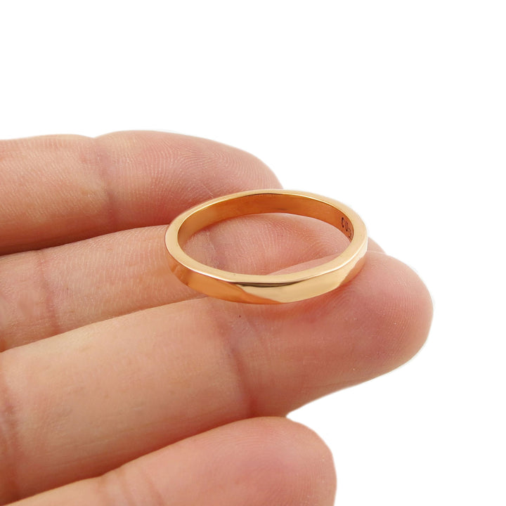 Solid polished copper jewellery ring held in a person's hand against a white background