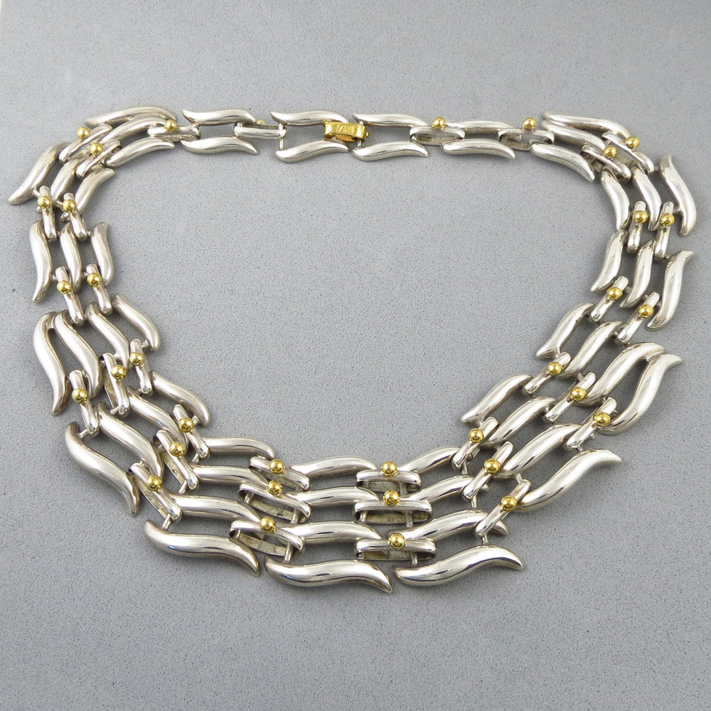 A wide Tane Mexico sterling 925 Silver collar necklace with gold accents on a gray background