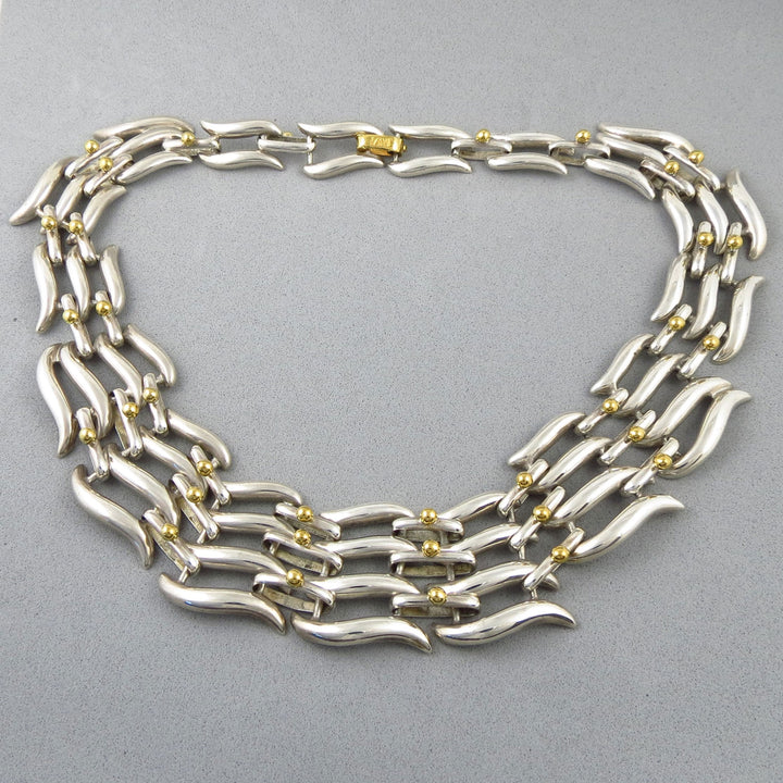 A wide Tane Mexico sterling 925 Silver collar necklace with gold accents on a gray background