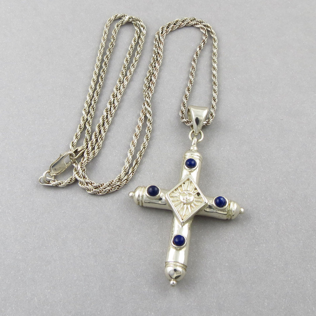 Mexican Sergio Bustamente sterling 925 silver ssun face cross pendant with blue lapis lazuli stones on a heavy rope chain against a gray background