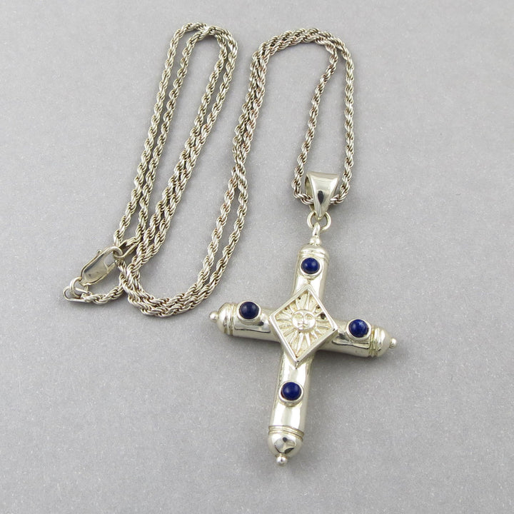 Mexican Sergio Bustamente sterling 925 silver ssun face cross pendant with blue lapis lazuli stones on a heavy rope chain against a gray background