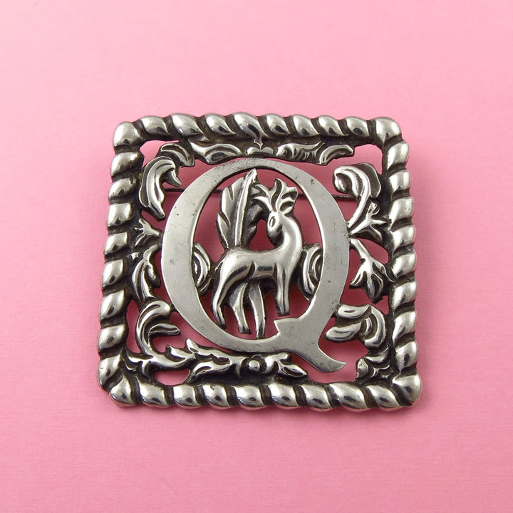 A vintage Fred Davis Mexican sterling 925 Silver decorative brooch with the letter 'Q' and a deer on a pink background