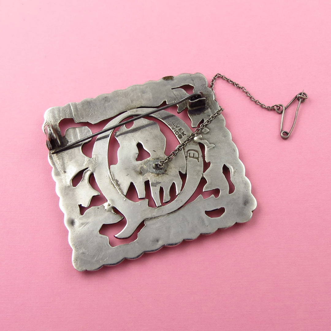Decorative silver brooch with intricate design and Fred Davis Mexico Silver hallmark on a pink background