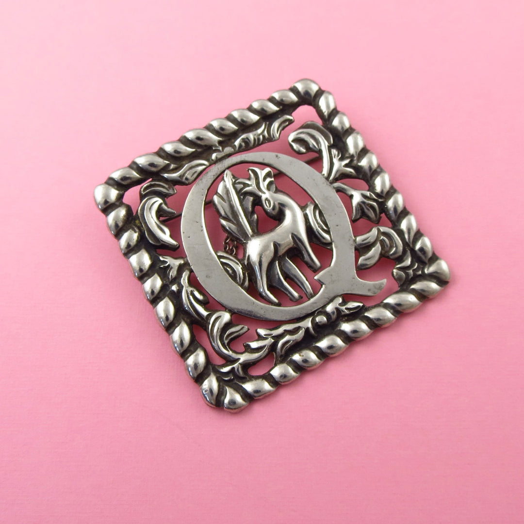 Vintage Fred Davis Mexican Sterling 925 Silver decorative brooch with a deer design and letter Q on a pink background