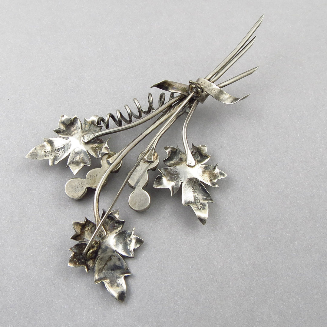 A large vintge 925 sterling silver leaf and flowers brooch upsside down on a gray background