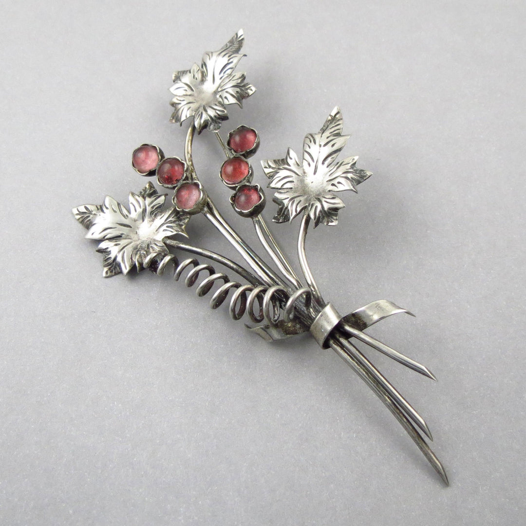 Vintage Taxco Mexico Sterling 925 Silver brooch with floral design and pink gemstones on a gray background