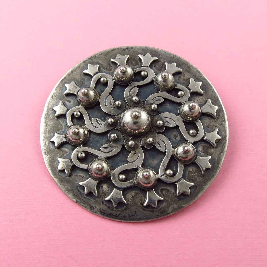 Mexican Sterling silver Los Castillo brooch with intricate pre-columbian aztec flower design on a pink background