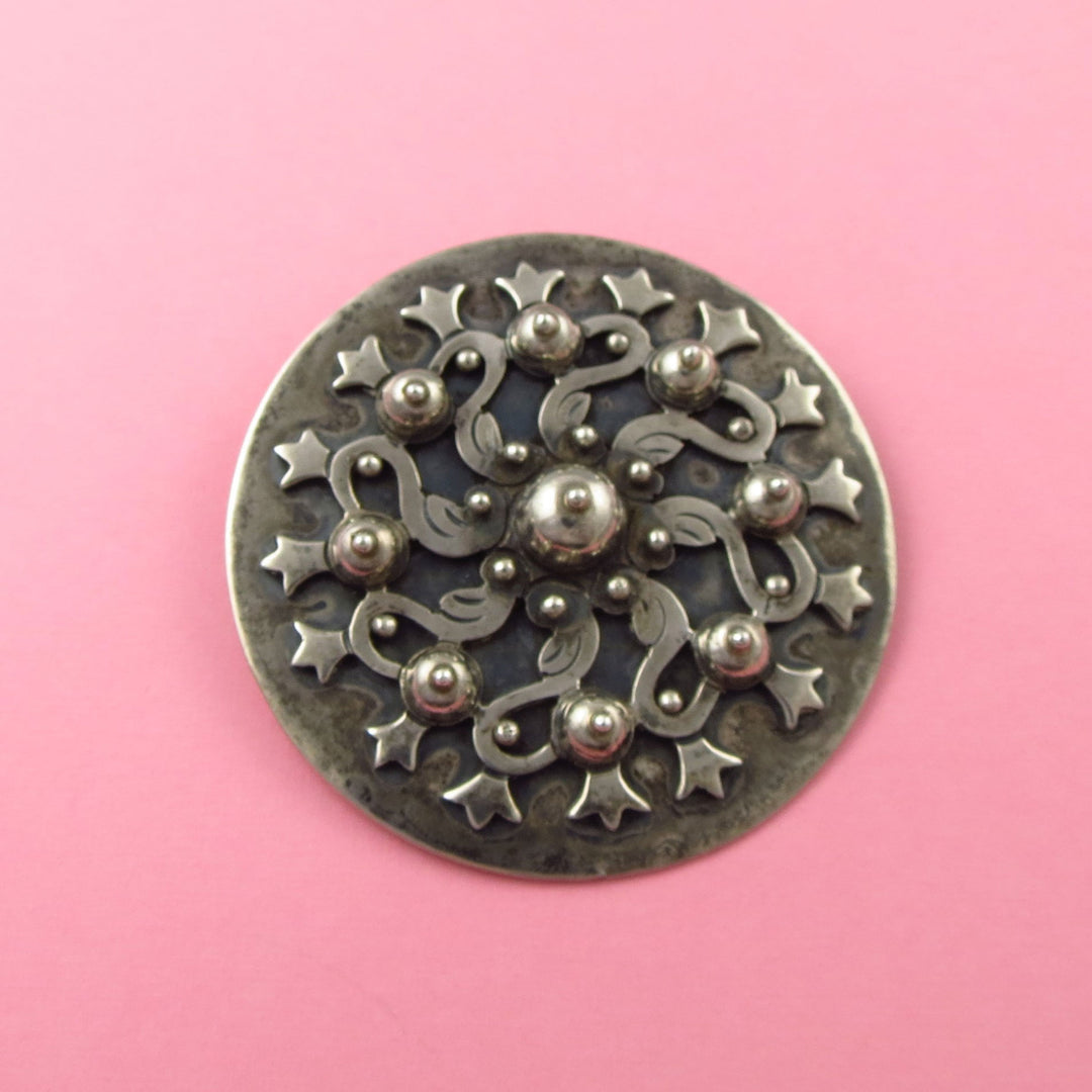 A large vintage sterling 925 silver Los Castillo old Taxco design circle brooch on a pink background
