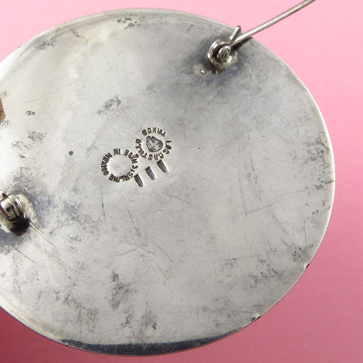 Close-up of a vintage Taxco sterling silver brooch that shows the Los Castillo hallmark on a pink background