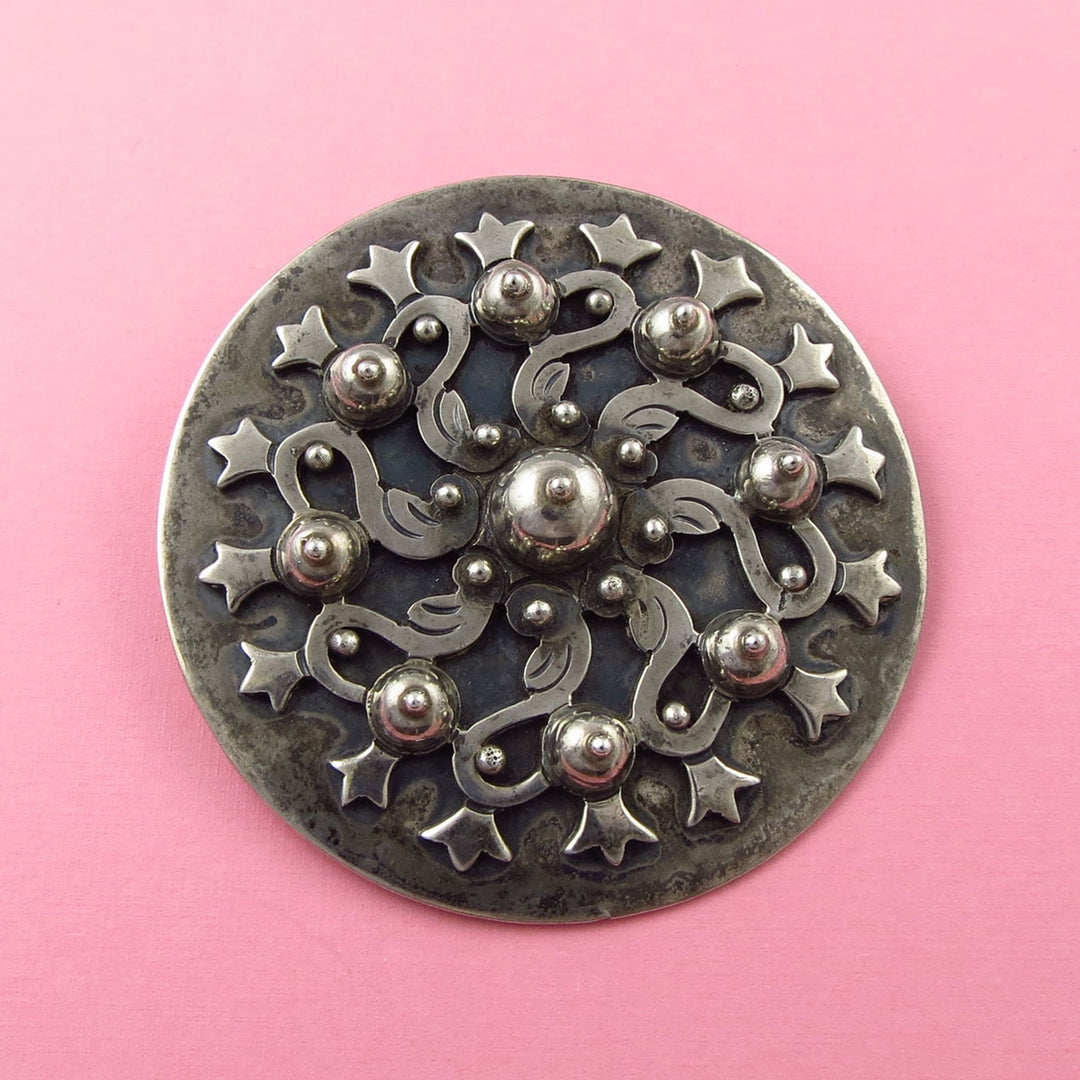 Large vintage Los Castillo Meixcan sterling silver aztec flower brooch on a pink background