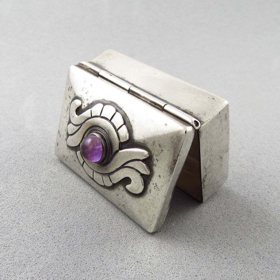 A vintage Damaso Gallegos Taxco Mexican 925 Silver box with a purple amethyst gemstone on a gray background