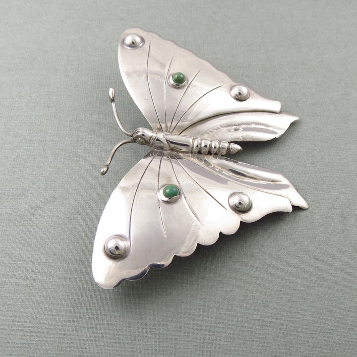 Handmade sterling 925 silver Monarch butterfly brooch with green turquoise gemstones on a gray background