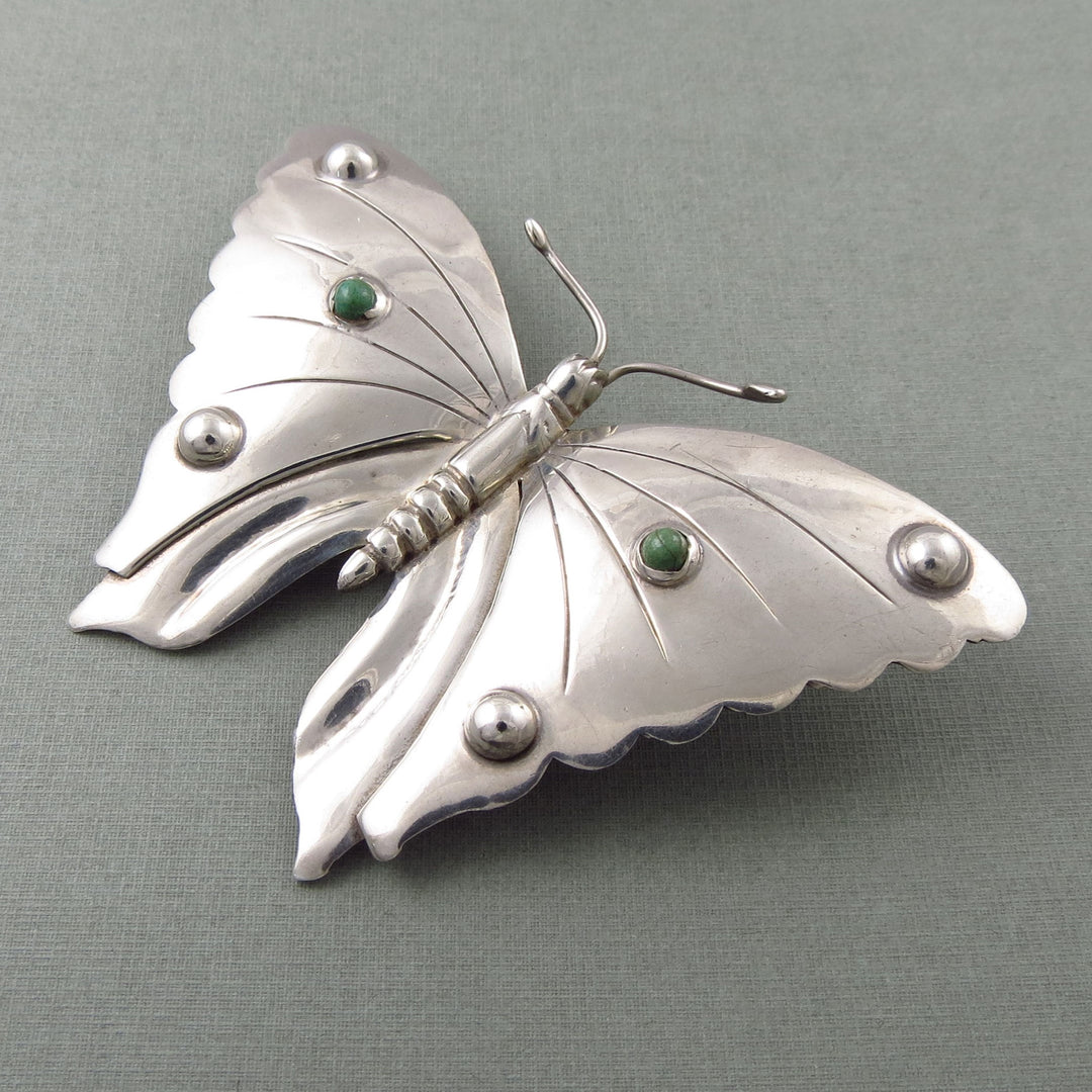 Sterling 925 Silver monarch butterfly brooch with green turquoise gemstones on a grey background