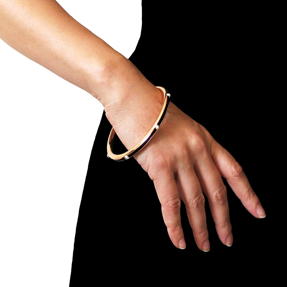 Woman wearing a unique copper and silver mixed metal bangle on her wrist against a black dress