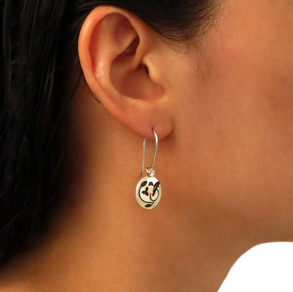 A dangling 925 silver earring with a nightingale silhouette design worn by a woman with dark hair