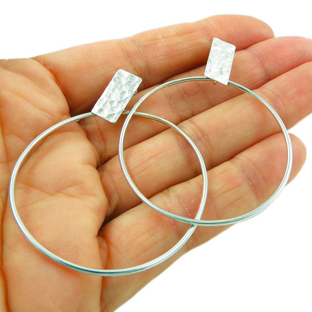 Hand holding a pair of solid Mexican 925 silver circle hoop earrings UK against a white background.