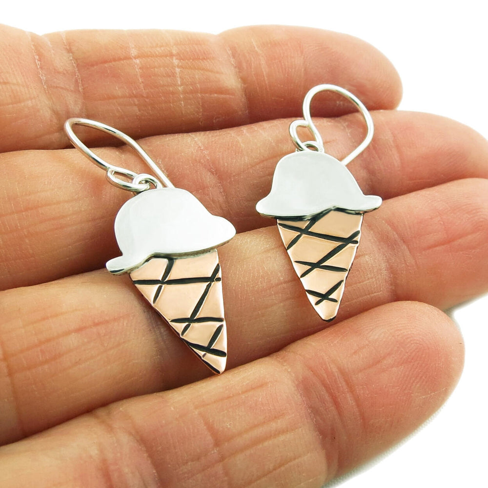 A pair of ice cream cone earrings made of silver and copper, displayed on a person's hand.