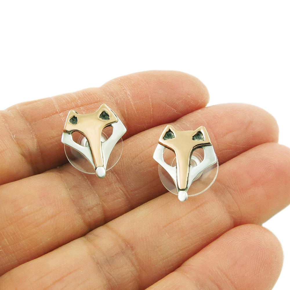 A pair of sterling silver and copper animal fox countryside earrings held in a person's hand.