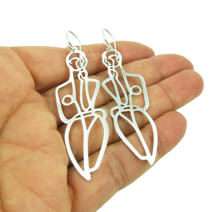 Large drop earrings in 925 sterling silver that feature silhouettes of the female body held in a woman's hand on a white background.