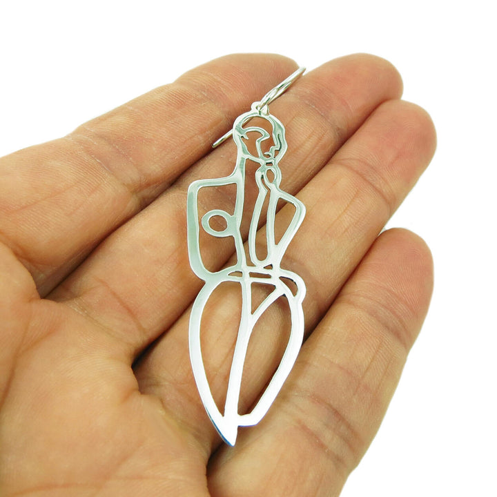 A single large 925 sterling silver earring in the shape of a female in a fashion pose held in a woman's hand on a white background. 
