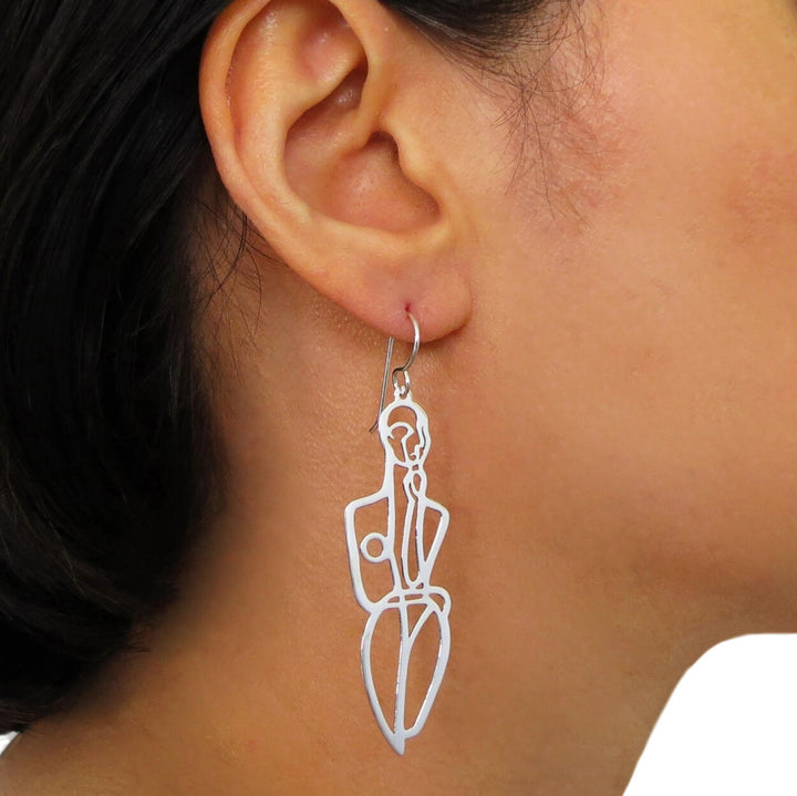 A large 925 silver drop earring in the shape of a woman striking a fashion pose worn by a female with dark hair. 
