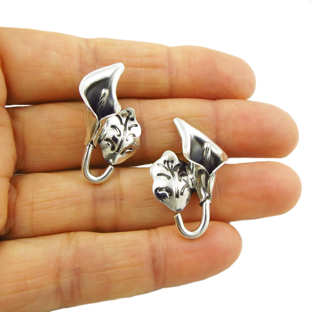 Mexican 925 sterling silver calla lily earrings for women show-cased between a person's fingers on a plain background. 