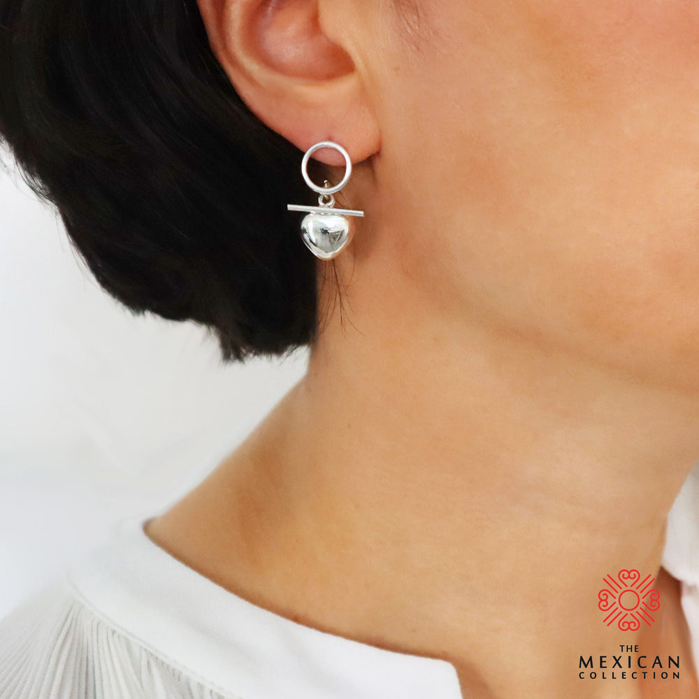 Silver puffed heart drop earrings worn by a woman with a white blouse