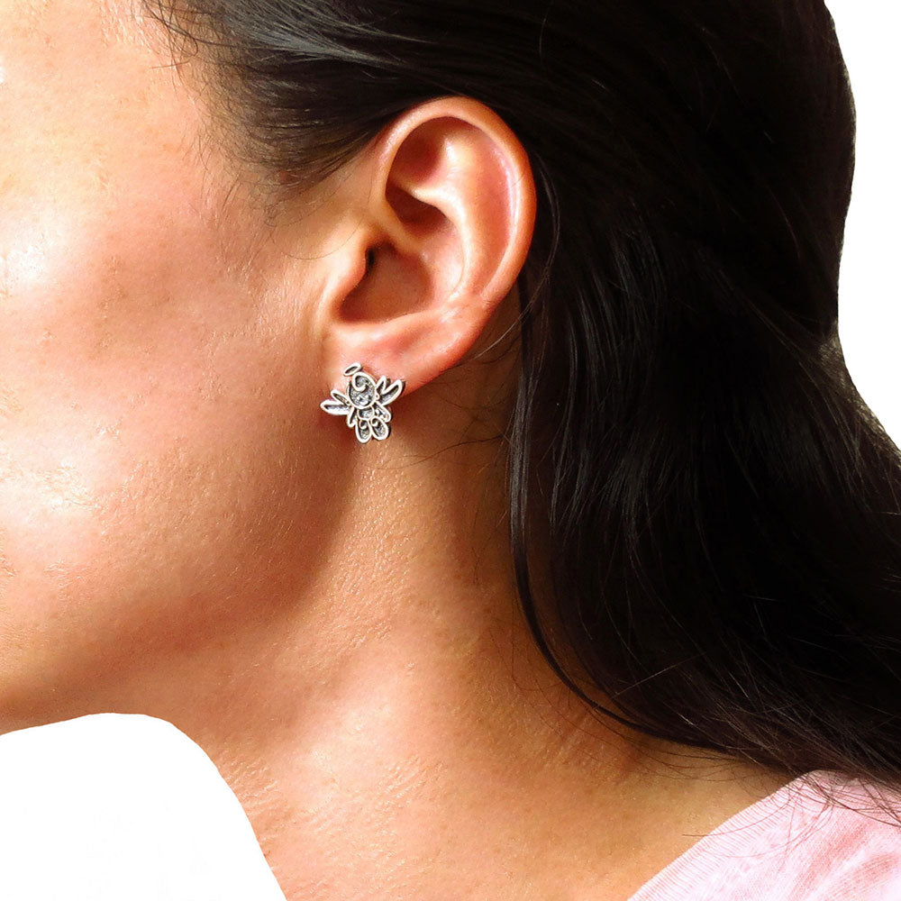 A large two tone 925 silver angel earring worn by a woman with dark hair