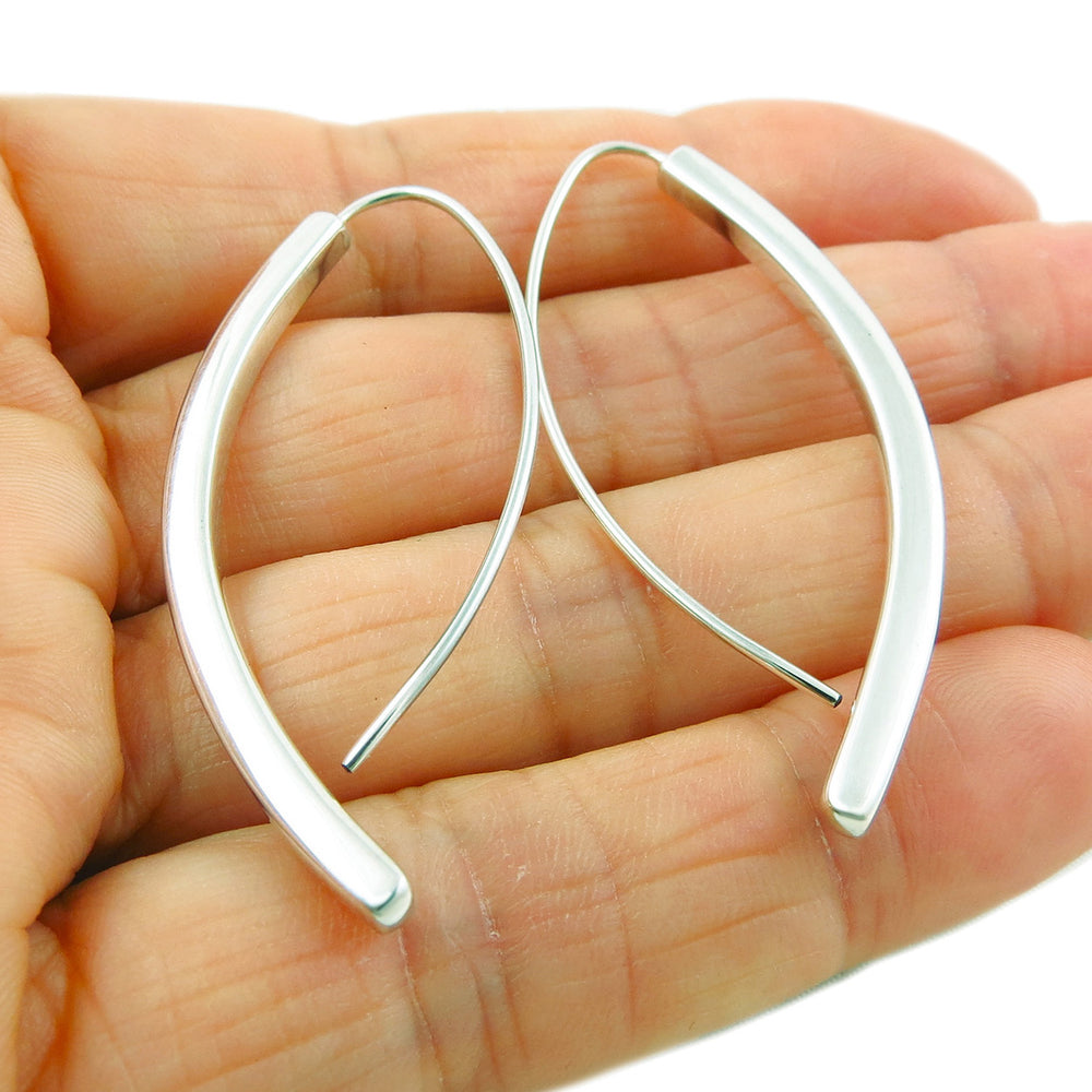 A pair of 925 sterling silver curved stick drop earrings held in a person's hand, showing the earrings' ability to drape in an inverted V shape.