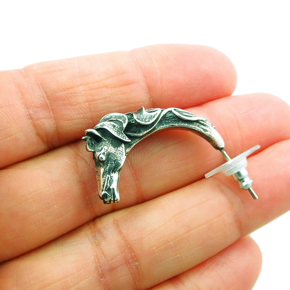 A large sculpted solid sterling 925 silver horse head half hoop earring held in a woman's hand on a white background. 
