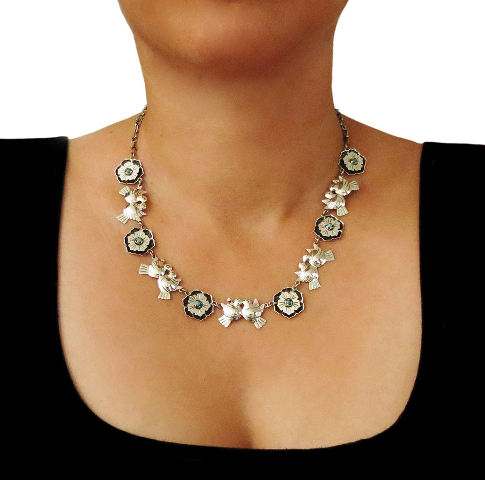 A woman in a black dress wearing a unique lovebird and flowers handmade 925 sterling silver Mexican Maria Belen Nilson necklace decorated with turquoise gemstones.