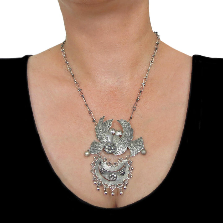 A large Mexican lovebird necklace in polished and antiqued sterling silver worn by a woman in a black top