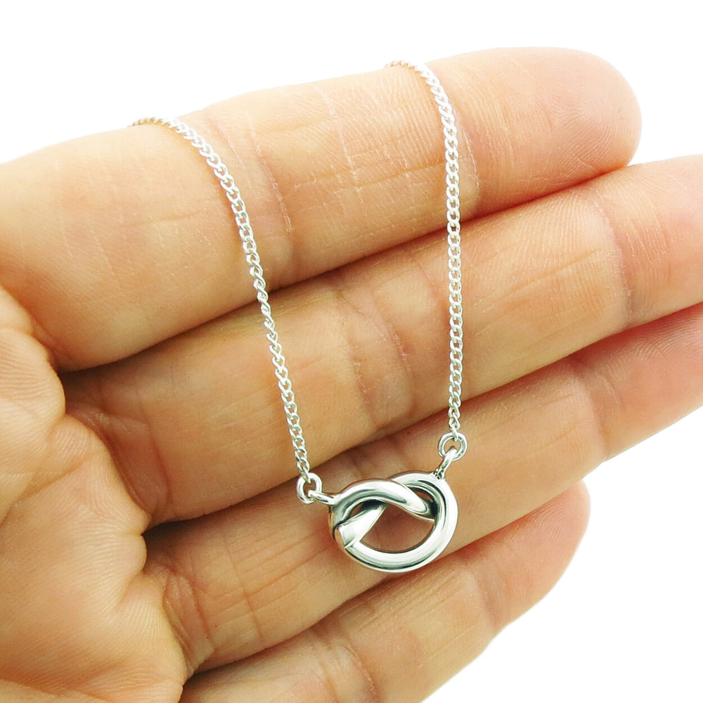 A hand holding a 925 sterling silver chain necklace with a love knot pendant.