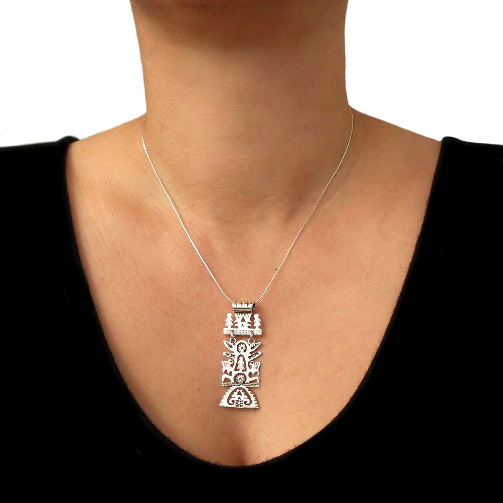 Silver tree of life pendant on a chain being worn by someone with a black top on a white background