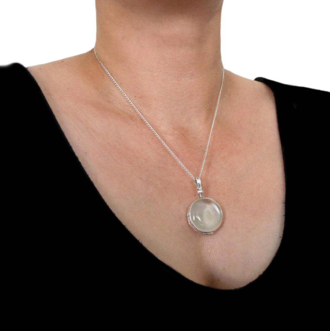 A large sterling 925 silver pendant locket hanging on a curb chain worn bya woman in a black top. 